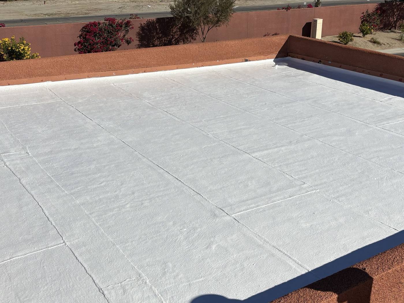 After: Flat roof with parapet walls, Worn, sun-cooked cap sheet sealed under a bright white reflective coating.