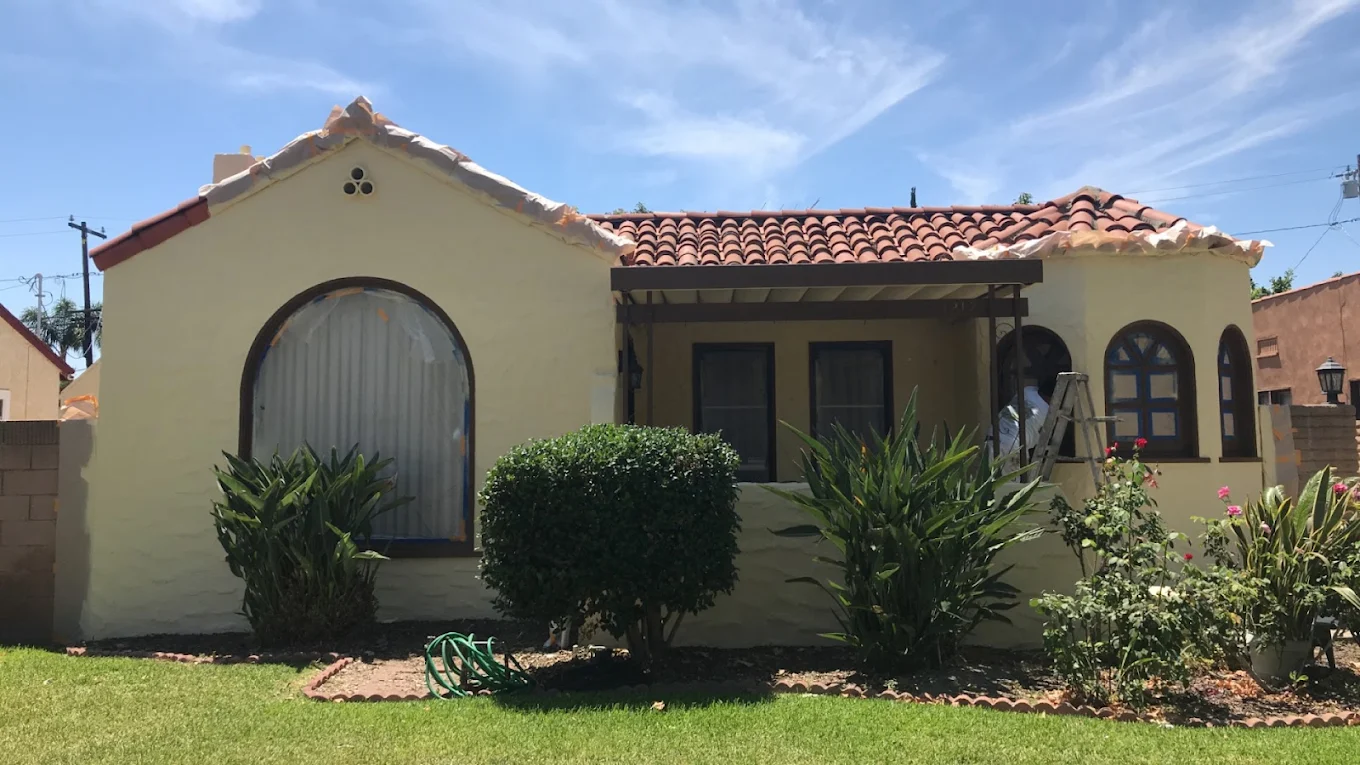 Single-story Spanish stucco home with brick wall and ironwork