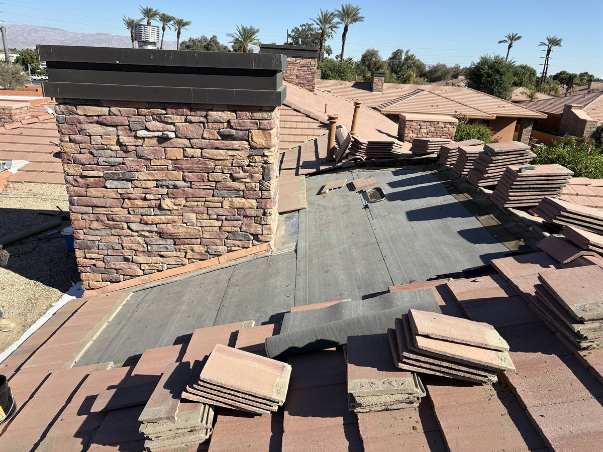 Tile re-roof in progress around a stone chimney detail