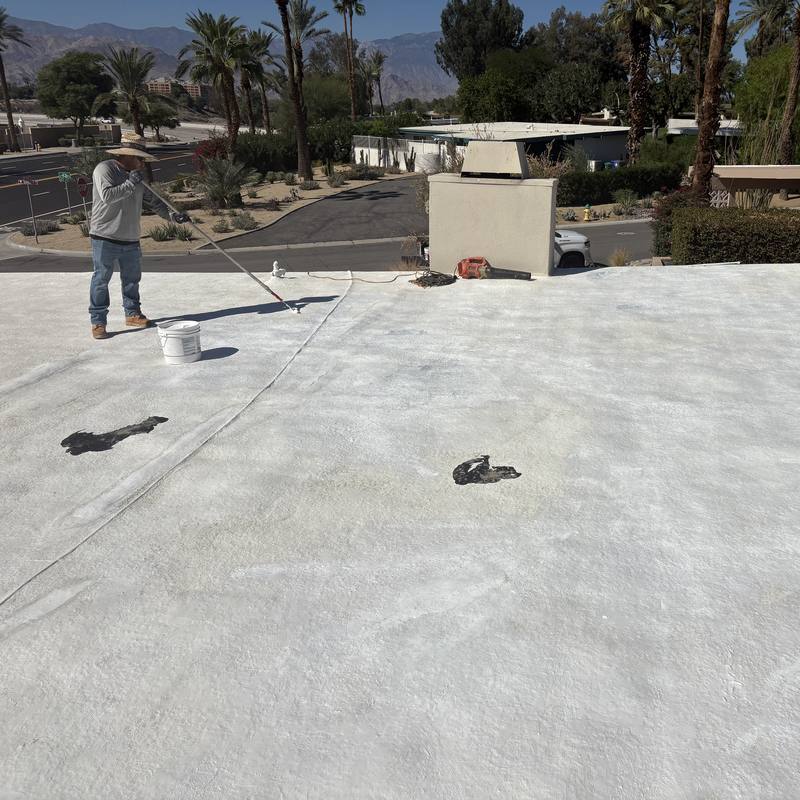Fresh coat on a foam roof: Our crew rolling a new white topcoat across a flat foam roof.