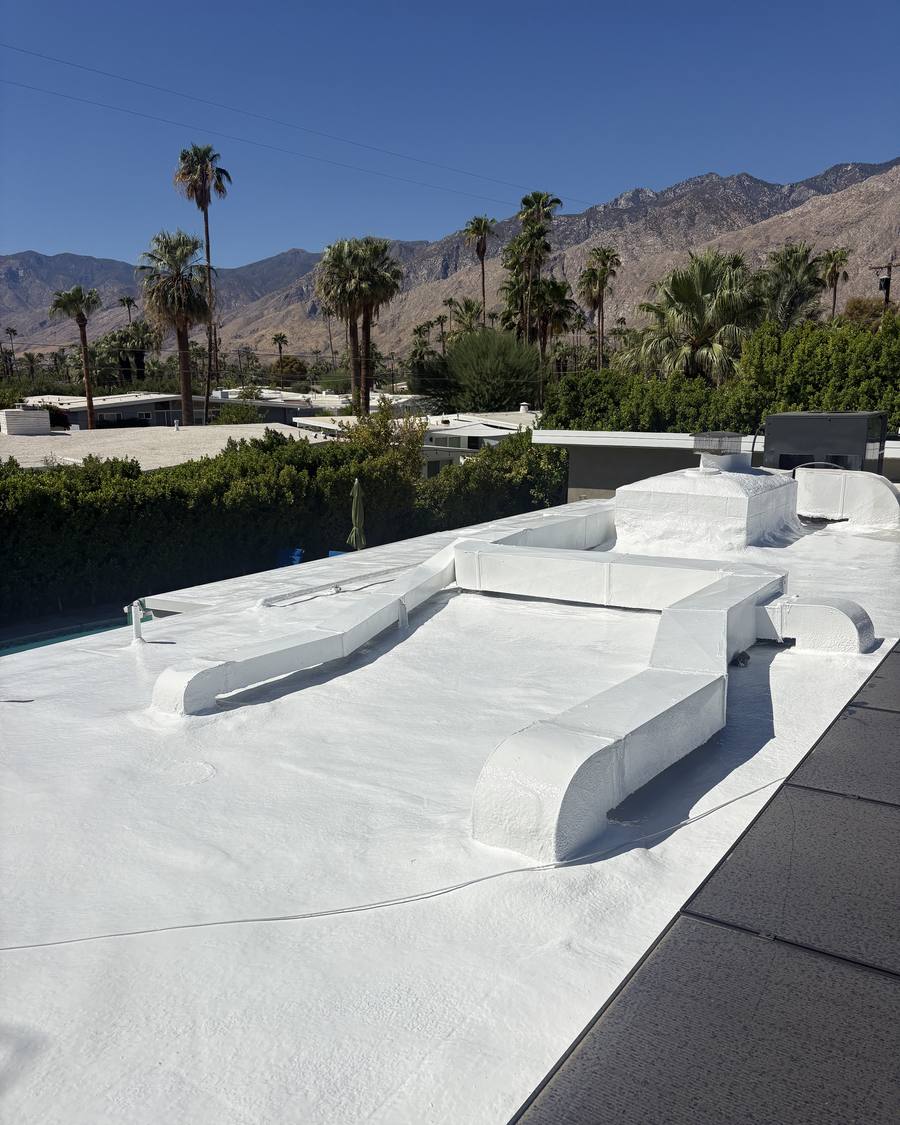 Finished white foam roof with ducts and parapets, desert mountains behind